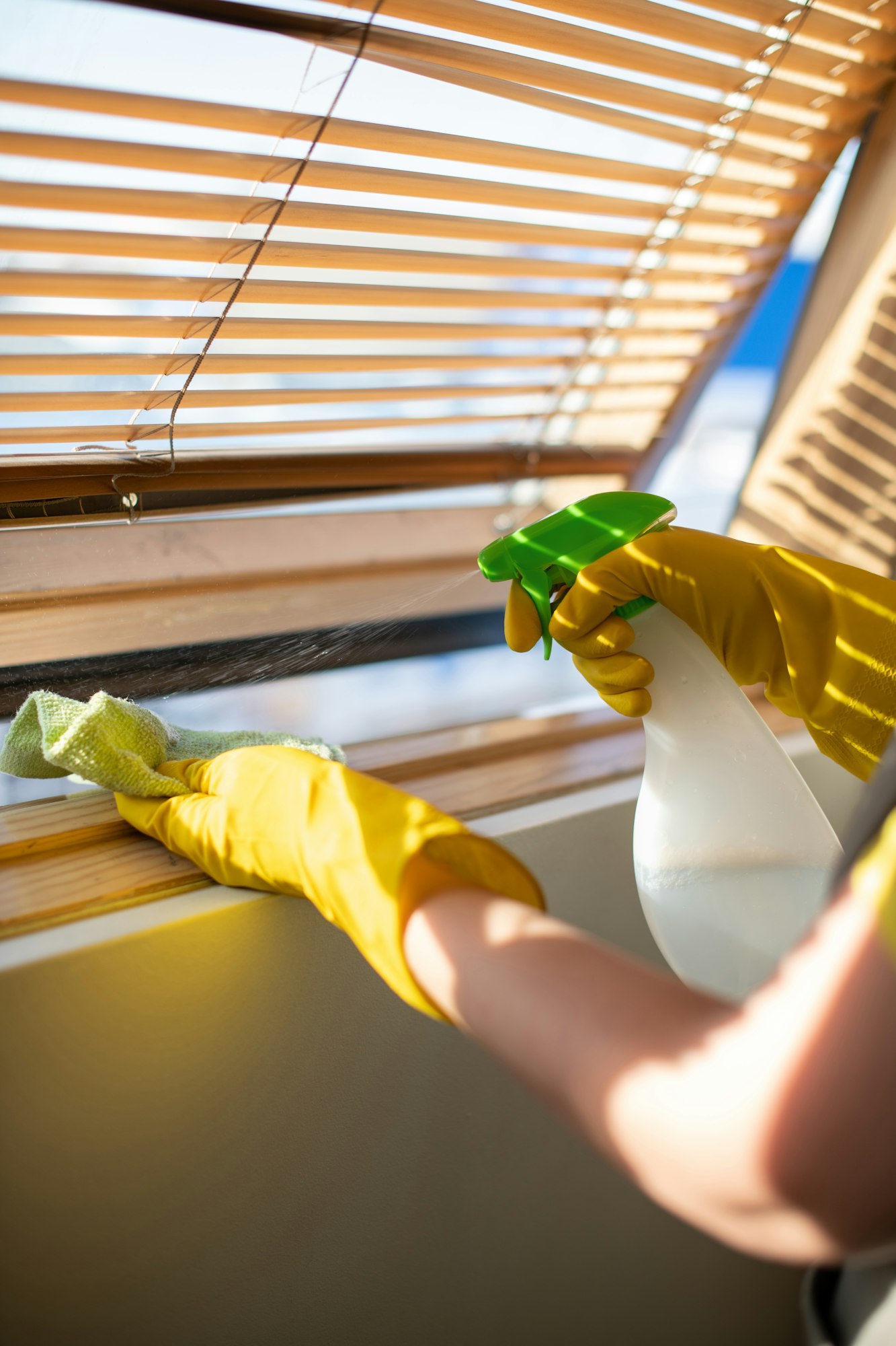 A woman in yellow rubber gloves washes the blinds