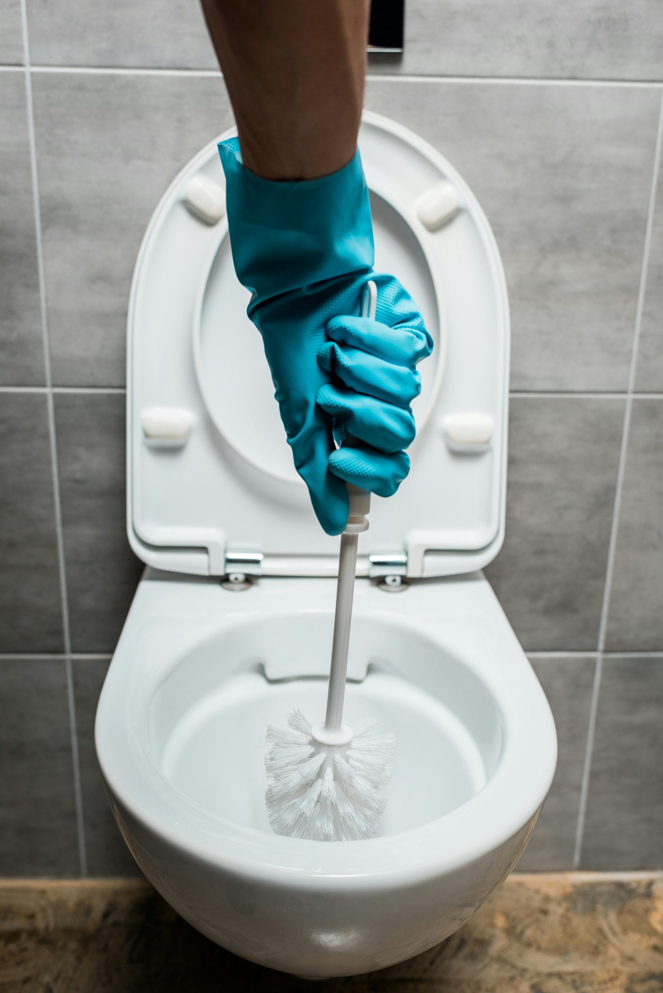 cropped view of cleaner cleaning ceramic toilet bowl with toilet brush in modern restroom with grey